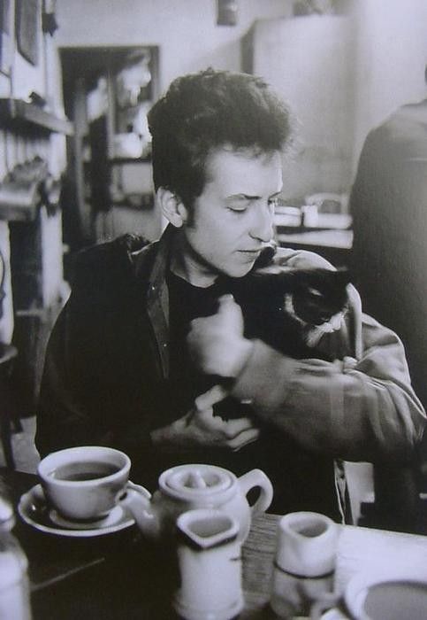 A black-and-white photo of Bob Dylan and a black and white cat. They appear to be in a diner. 